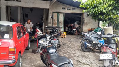 bengkel motor pak medek. terlihat pak medek dan karyawan sedang memperbaiki motor matic dan manual. terlihat banyak motor yang akan di perbaiki