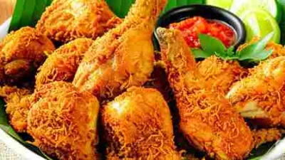 Sepiring ayam goreng lengkuas berwarna keemasan dengan taburan rempah lengkuas goreng yang renyah, disajikan dengan sambal merah dan potongan jeruk nipis di atas alas daun pisang.