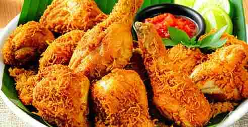 Sepiring ayam goreng lengkuas berwarna keemasan dengan taburan rempah lengkuas goreng yang renyah, disajikan dengan sambal merah dan potongan jeruk nipis di atas alas daun pisang.