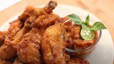 Potongan ayam goreng crispy disajikan dengan saus sambal dan jeruk limau