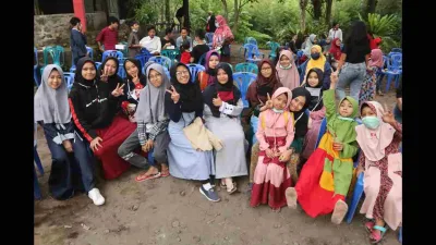 Anak-anak dan remaja berkumpul di sebuah kegiatan pendidikan alam di lereng Merapi, duduk bersama di kursi biru dengan suasana akrab dan penuh keceriaan.