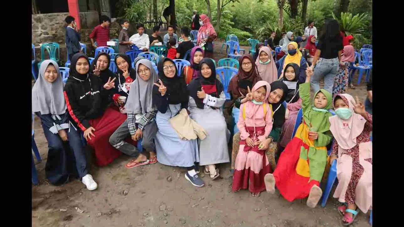 Anak-anak dan remaja berkumpul di sebuah kegiatan pendidikan alam di lereng Merapi, duduk bersama di kursi biru dengan suasana akrab dan penuh keceriaan.