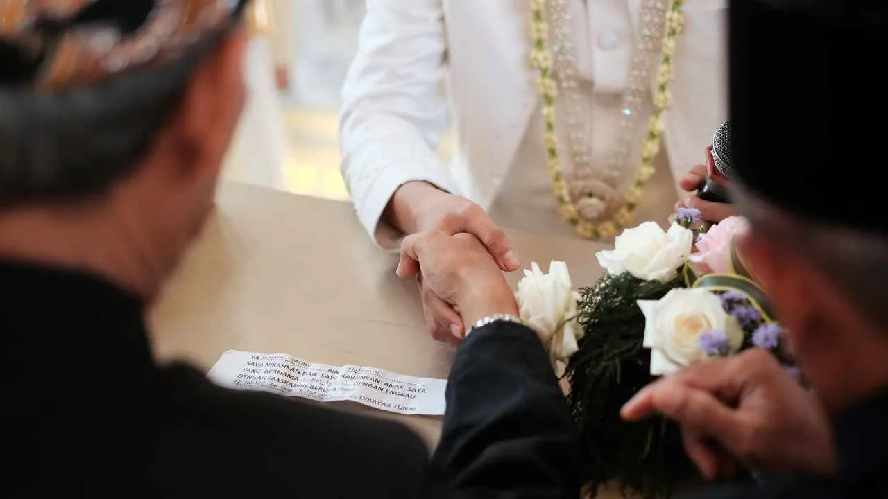 Prosesi akad nikah dengan berjabat tangan antara mempelai pria dan wali disaksikan penghulu.