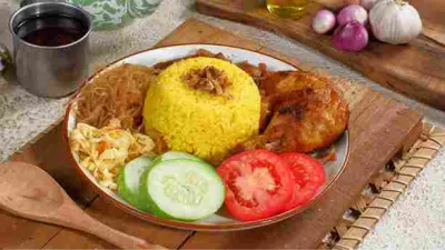 Nasi kuning gurih disajikan dengan ayam goreng, bihun, sambal goreng, irisan tomat, dan mentimun.