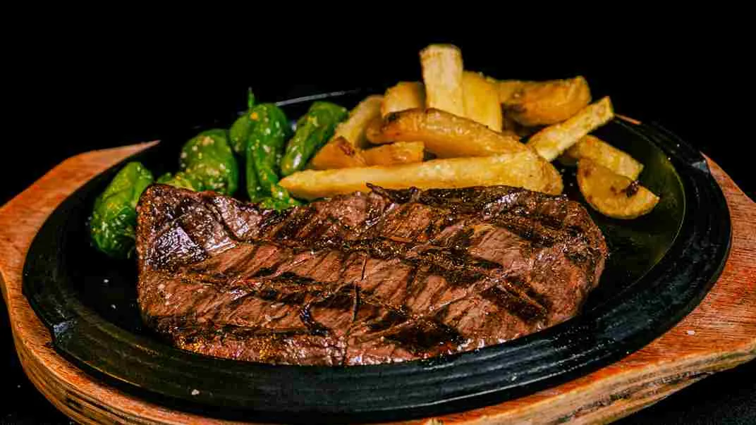 Steak ayam barbeque dengan kentang goreng dan sayuran hijau di atas hot plate
