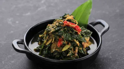 Tumis daun pepaya dengan cabai merah dan ikan teri gurih dalam mangkuk hitam.