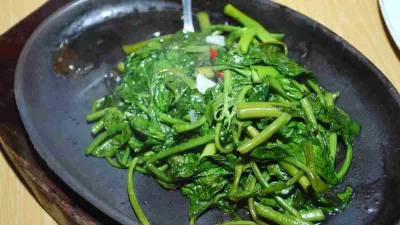 Tumis kangkung ala restoran disajikan di atas hotplate dengan bumbu bawang putih dan cabai.