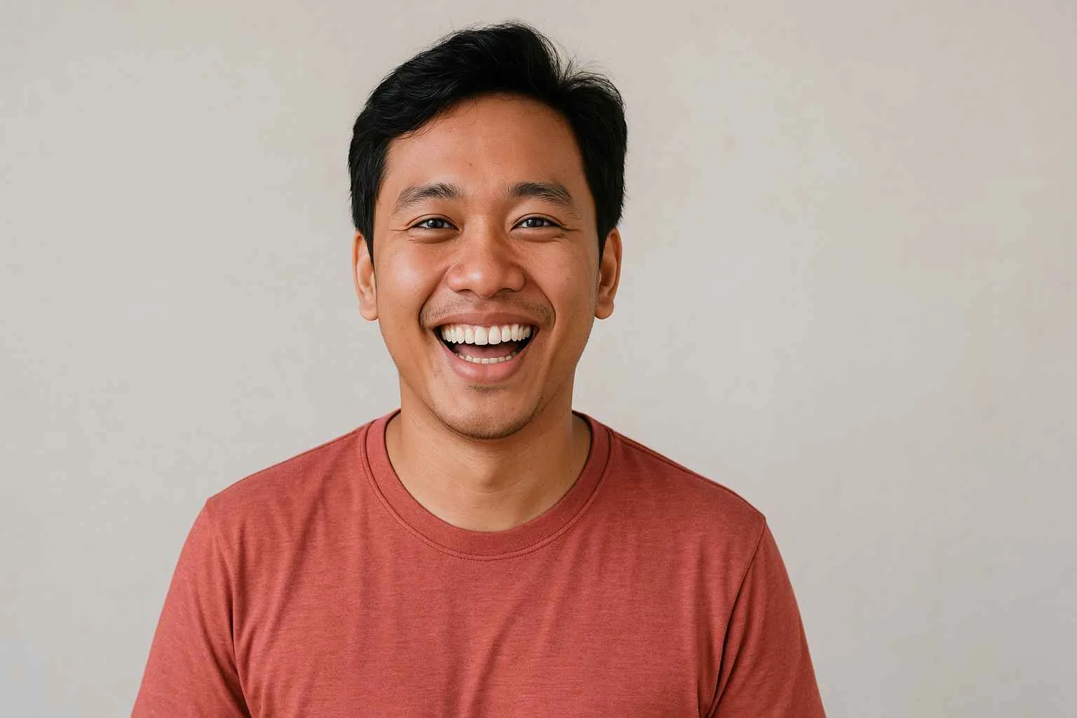 Pria muda Indonesia tersenyum lebar dengan ekspresi ceria mengenakan kaos merah.