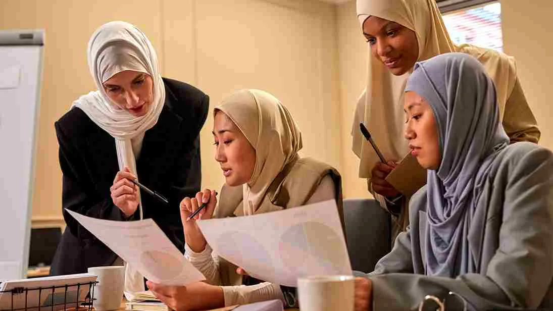 Sekelompok wanita berhijab sedang berdiskusi dan menganalisis grafik di ruang kerja modern.