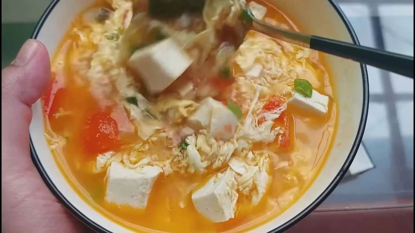 Sup tahu telur tomat hangat dengan kuah gurih segar, potongan tahu putih, telur serabut, dan irisan tomat merah.