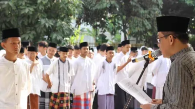 Seorang pembina membacakan amanat upacara Hari Santri Nasional 2025 di Sleman, di hadapan para santri yang mengenakan sarung dan peci hitam.