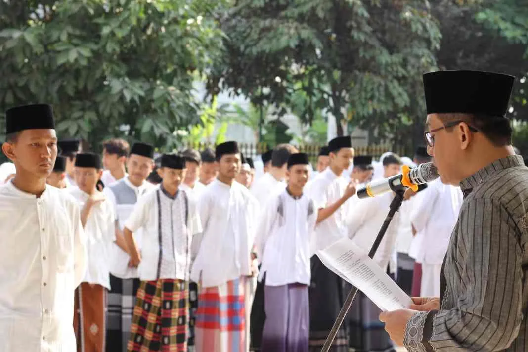 Seorang pembina membacakan amanat upacara Hari Santri Nasional 2025 di Sleman, di hadapan para santri yang mengenakan sarung dan peci hitam.