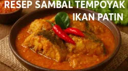 Sambal tempoyak ikan patin khas Sumatera disajikan dalam mangkuk tanah liat dengan kuah merah keemasan, dihiasi cabai merah dan daun jeruk segar.