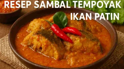 Sambal tempoyak ikan patin khas Sumatera disajikan dalam mangkuk tanah liat dengan kuah merah keemasan, dihiasi cabai merah dan daun jeruk segar.