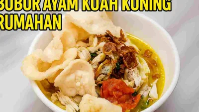 Bubur ayam kuah kuning rumahan disajikan dalam mangkuk putih dengan topping ayam suwir, sambal, bawang goreng, dan kerupuk renyah di atas meja marmer.