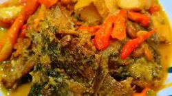 Ikan nila tauco tahu dengan kuah kuning gurih dan potongan cabai merah disajikan di piring putih di atas meja kayu.