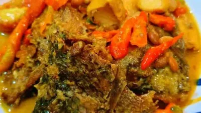 Ikan nila tauco tahu dengan kuah kuning gurih dan potongan cabai merah disajikan di piring putih di atas meja kayu.