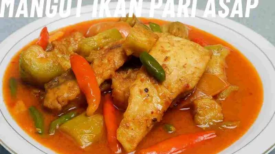 Mangut ikan pari asap dengan kuah santan pedas berwarna merah oranye, disajikan di atas piring putih bersama potongan terong dan cabai merah hijau.