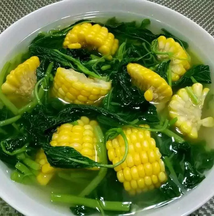 Semangkuk sayur bening bayam jagung manis dengan kuah jernih, berisi potongan jagung muda dan daun bayam segar.