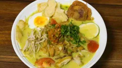 Semangkuk Soto Ayam Medan lengkap dengan telur rebus, perkedel, tauge, sambal, dan irisan jeruk nipis disajikan di atas piring putih dengan kuah kuning santan gurih di atas meja kayu.