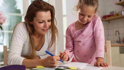 Ibu membantu anak belajar sambil berbicara dengan lembut di meja belajar.