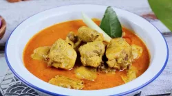 Kari ayam kuah santan berwarna kuning kemerahan dalam mangkuk putih, disajikan dengan potongan ayam, serai, dan daun jeruk.