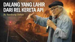 Rudolf Puspa, dalang dan seniman teater, berbicara sambil memegang mikrofon dengan latar rel kereta api simbol perjuangan dan seni
