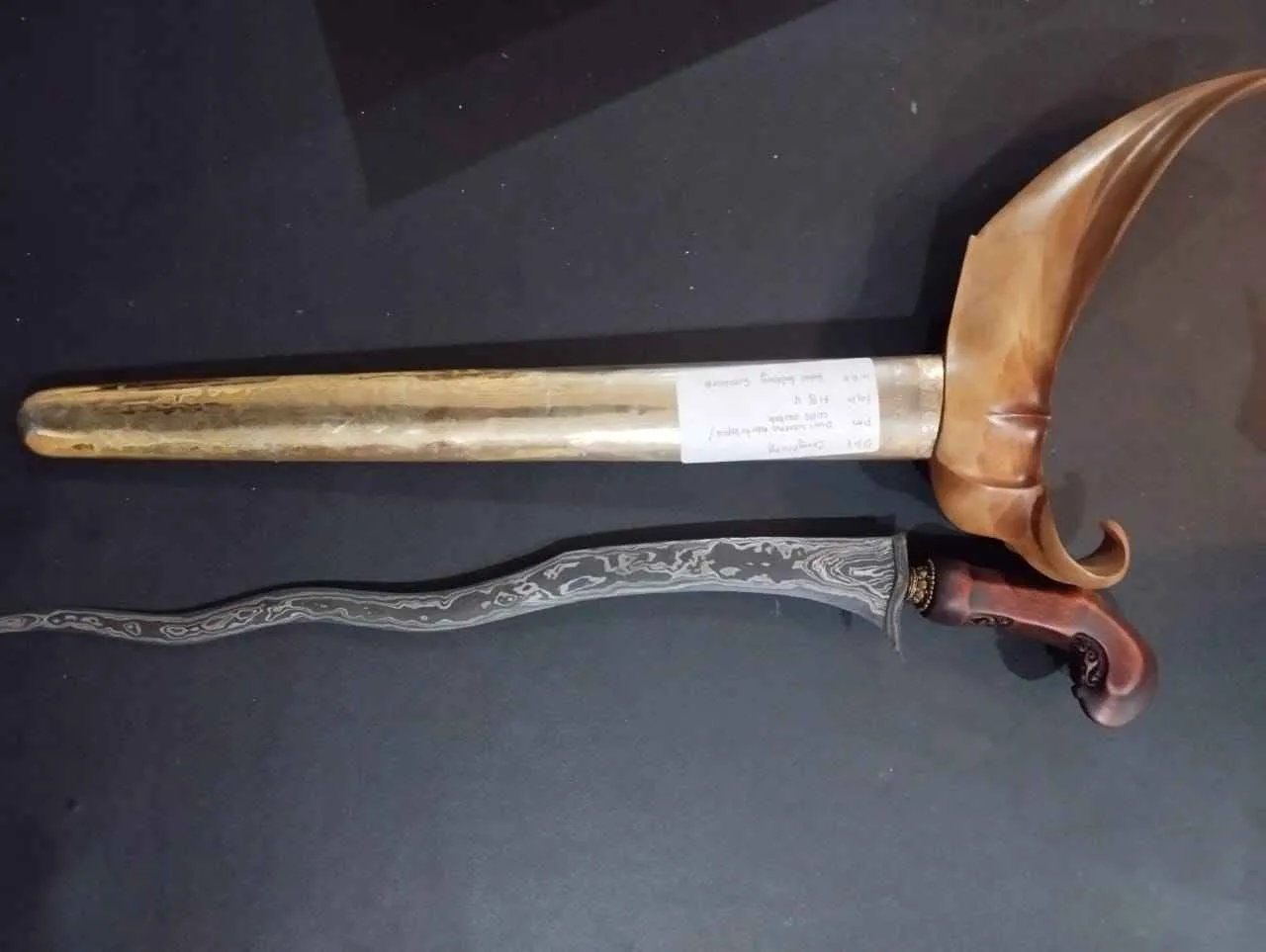 Keris Jawa dengan pamor berpola mengalir pada bilah, lengkap dengan warangka dan gagang kayu ukir tradisional.